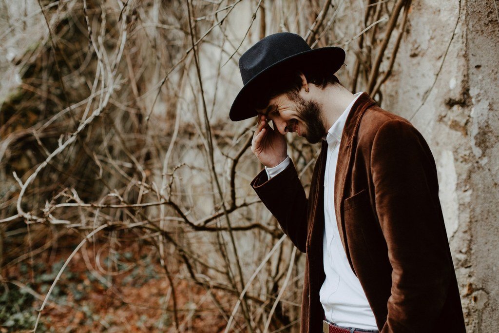 Le marié porte un chapeau noir et une belle veste en velours marron.